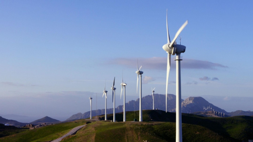 Sieben Windräder inmitten einer Hügellandschaft. Im Hintergrund befinden sich weitere