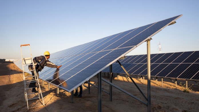 Arbeiter steht auf einer Leiter und lehnt sich über ein Solarpanel, um daran zu arbeiten