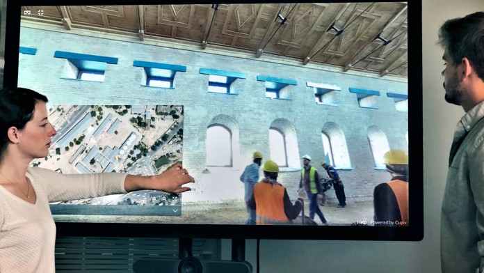 Two colleagues stand in front of a screen on which they are looking at a construction site of a building in Kabul