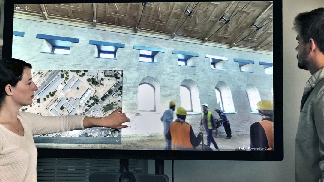 zwei Kollegen stehen vor einem Bildschirm auf dem sie auf eine Baustelle eines Gebäudes in Kabul schauen