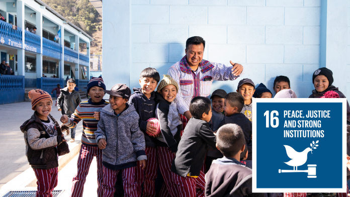 Happy children with their teacher in a school in Guatemala, next to them the SDG16-Icon: Peace, justice and strong institutions