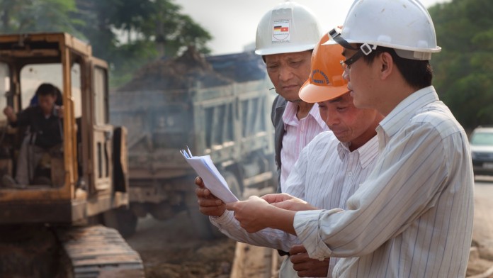 Asiatische Bauarbeiter und Ingenieure beugen sich über Karten.