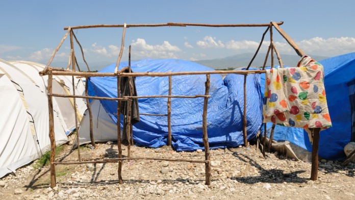 A tent frame built from wooden poles without fabric. On the side hangs a colourful ceiling