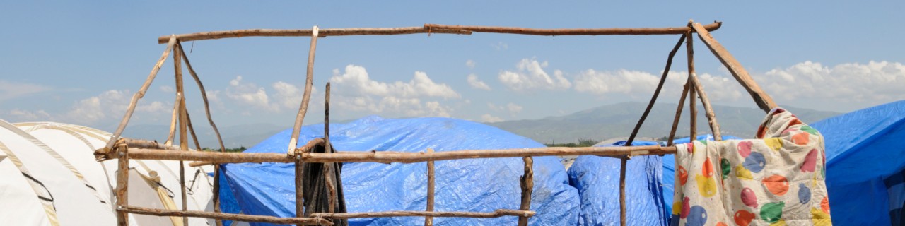 Ein Zeltgerüst aus Holz ohne Stoff inmitten von Flüchtlingszelten