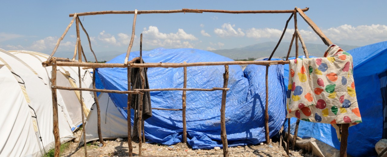 Ein Zeltgerüst aus Holz ohne Stoff inmitten von Flüchtlingszelten