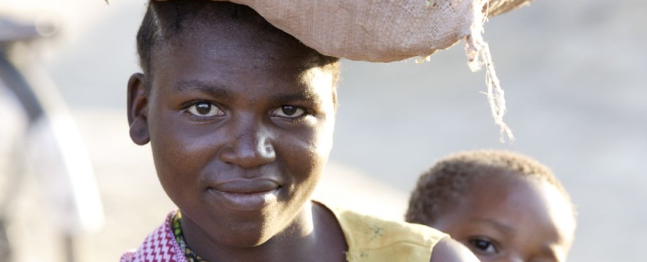 Woman with her child on her back is carrying a bag on her head