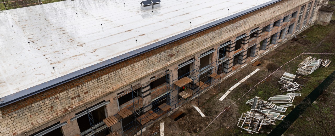 Construction site of a building without windows and partially scaffolded. The old windows lie in a heap in front of the building.