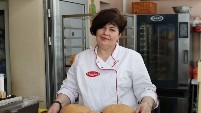 Baker with a tray full of bread in her hands.