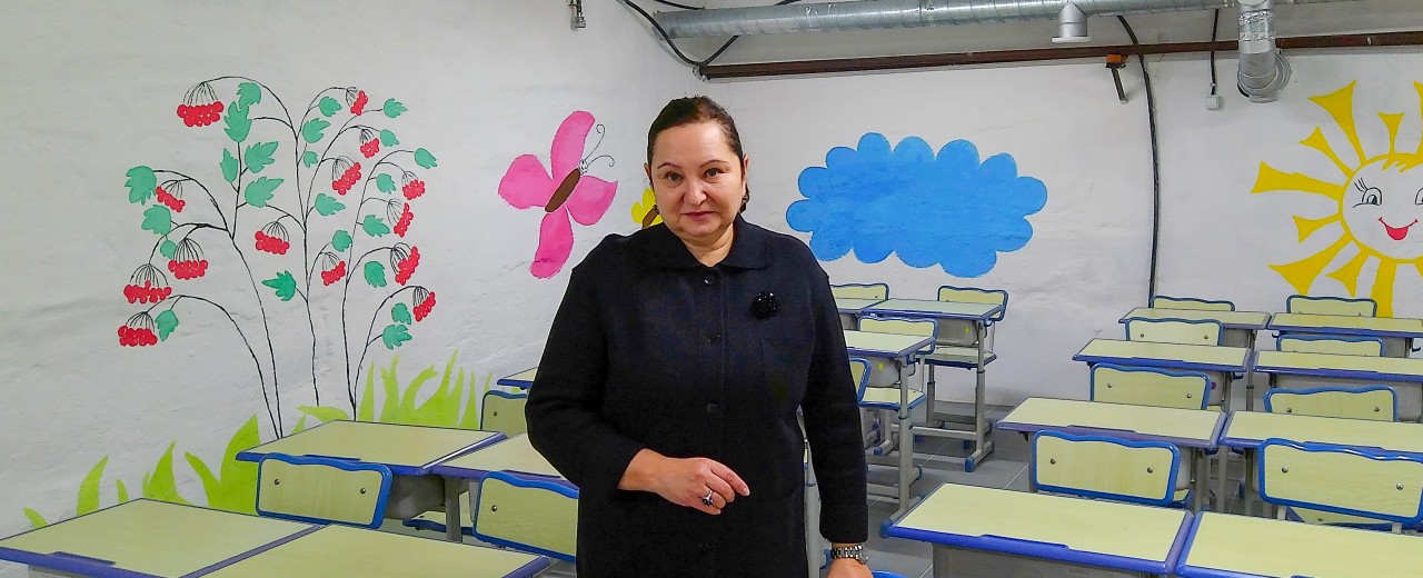 The gymnasium director is standing in a classroom in the bomb shelter.