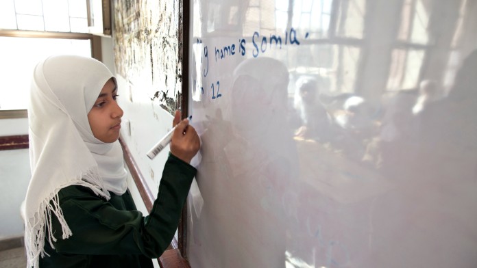 Schoolgirl wearing white headscarf writes mathematical formulas on a school blackboard
