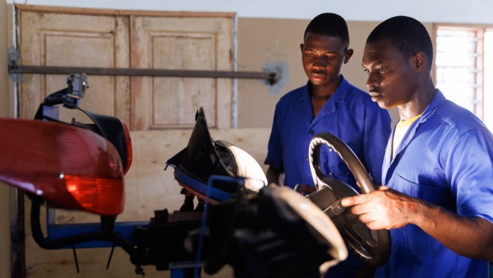 Two automotive mechanic apprentices in front of a training object.