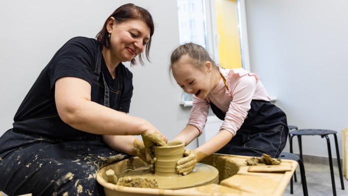 Workshop leader and child with Down's syndrome making pottery